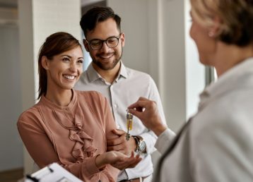 Young happy couple receiving new house keys from real estate age